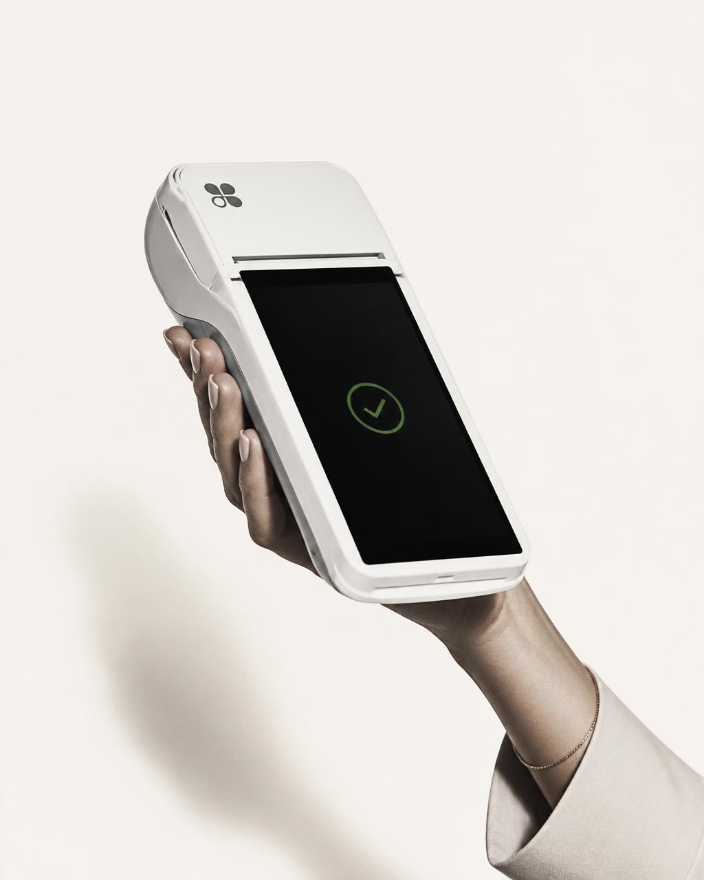 A hand holding a modern payment terminal displaying a successful transaction checkmark